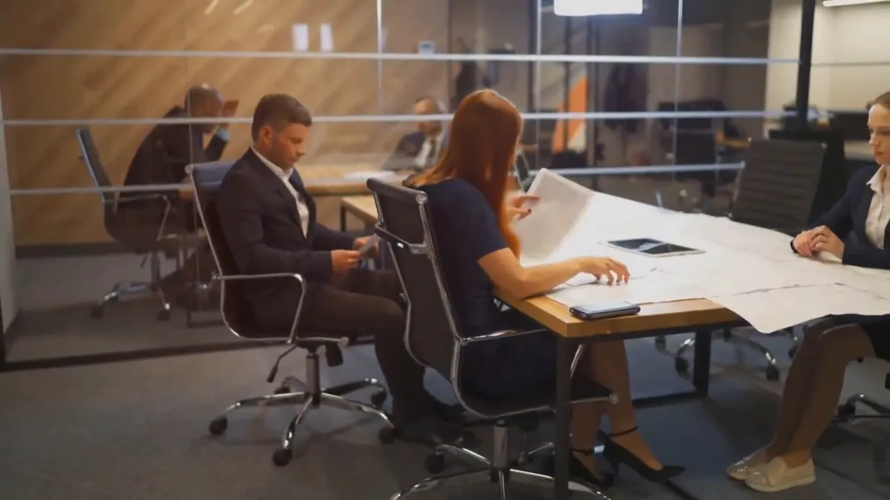 Business team reviewing plans at a conference table in an office with glass walls