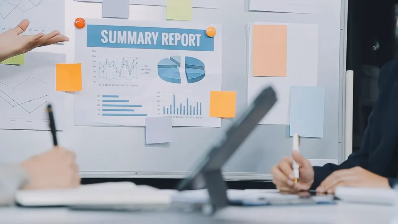 Clear view of a 'SUMMARY REPORT' pinned to a whiteboard with team members' hands taking notes in the foreground.